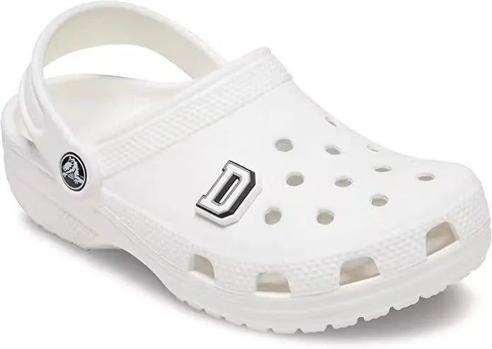 A glow-in-the-dark letter D Jibbitz charm attached to a Crocs shoe. Close-up of a white letter D Jibbitz with a green glow-in-the-dark outline on a Crocs clog. Dubailist glow-in-the-dark letter D Jibbitz charm, perfect for personalizing Crocs shoes and sandals.