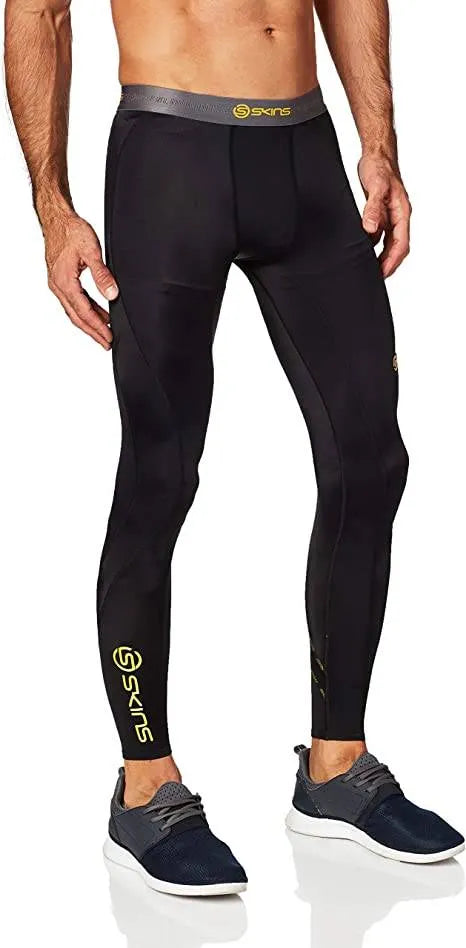 A male athlete wearing black and white Skins DNAmic Long Tights running confidently outdoors in snowy weather.