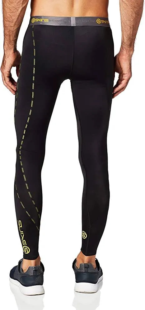 A male athlete wearing black and white Skins DNAmic Long Tights running confidently outdoors in snowy weather.