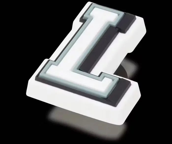 Glow-in-the-dark letter L Jibbitz charm for Crocs shoes. The letter L glows green in the dark. It is attached to a white Crocs shoe with ventilation holes.