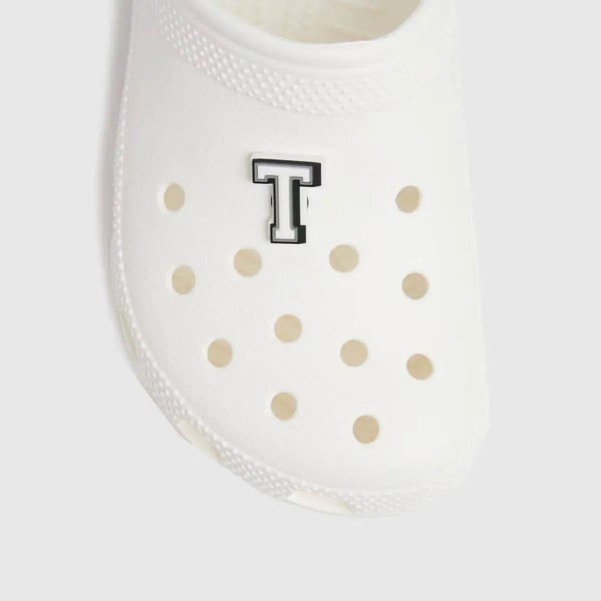 Crocs Glow-in-the-Dark Letter T Jibbitz, attached to a white Crocs shoe. The letter T glows brightly in the dark.