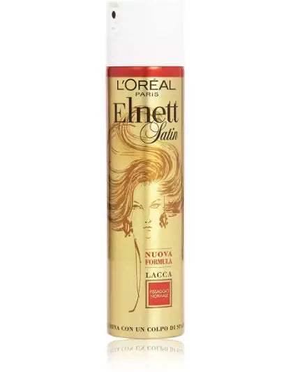 Silver can of L'Oreal Paris Elnett Micro Hairspray (250ml) with a pink nozzle and the text "Normal Hold with Precision Mist." A hand is spraying the hairspray onto styled hair.