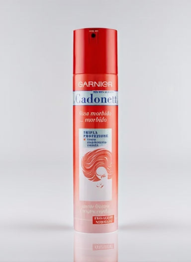 Canister of Garnier Micro-Aerated Cadonett hairspray (250ml) with a pink and silver design. A woman is using the spray to style her hair, with a focus on the flexible hold it offers.