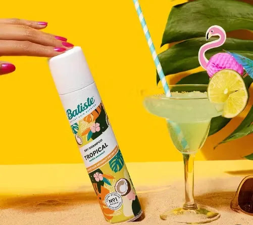 Canister of Batiste Dry Shampoo (200ml) in tropical design with a palm tree and coconut. A puff of powder is dispersing from the nozzle.