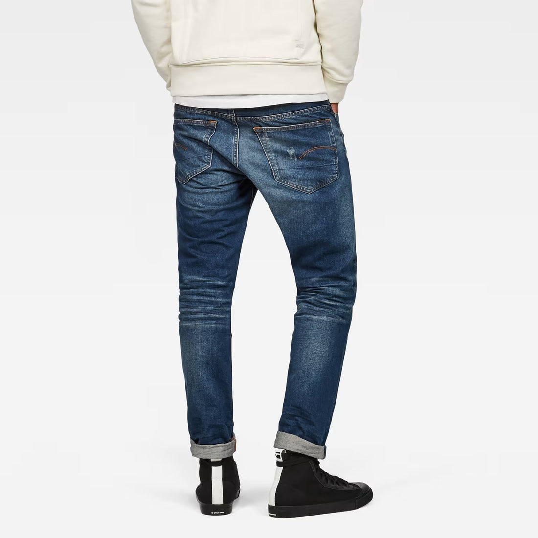 Back view of dark blue tapered jeans featuring distressed details on a white background.
