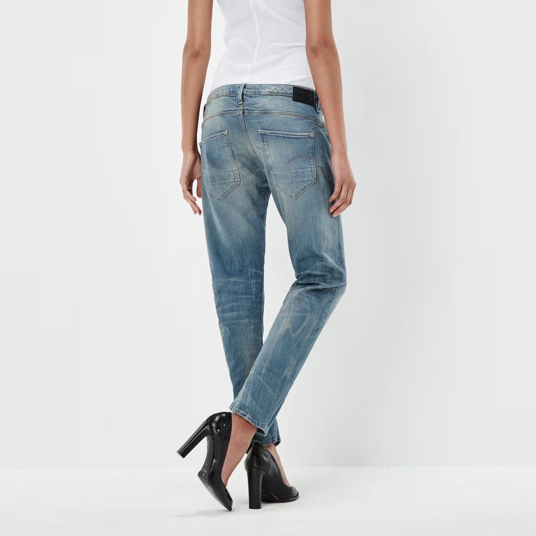 Back view of medium blue boyfriend jeans featuring a low waist and distressed look against a white background.