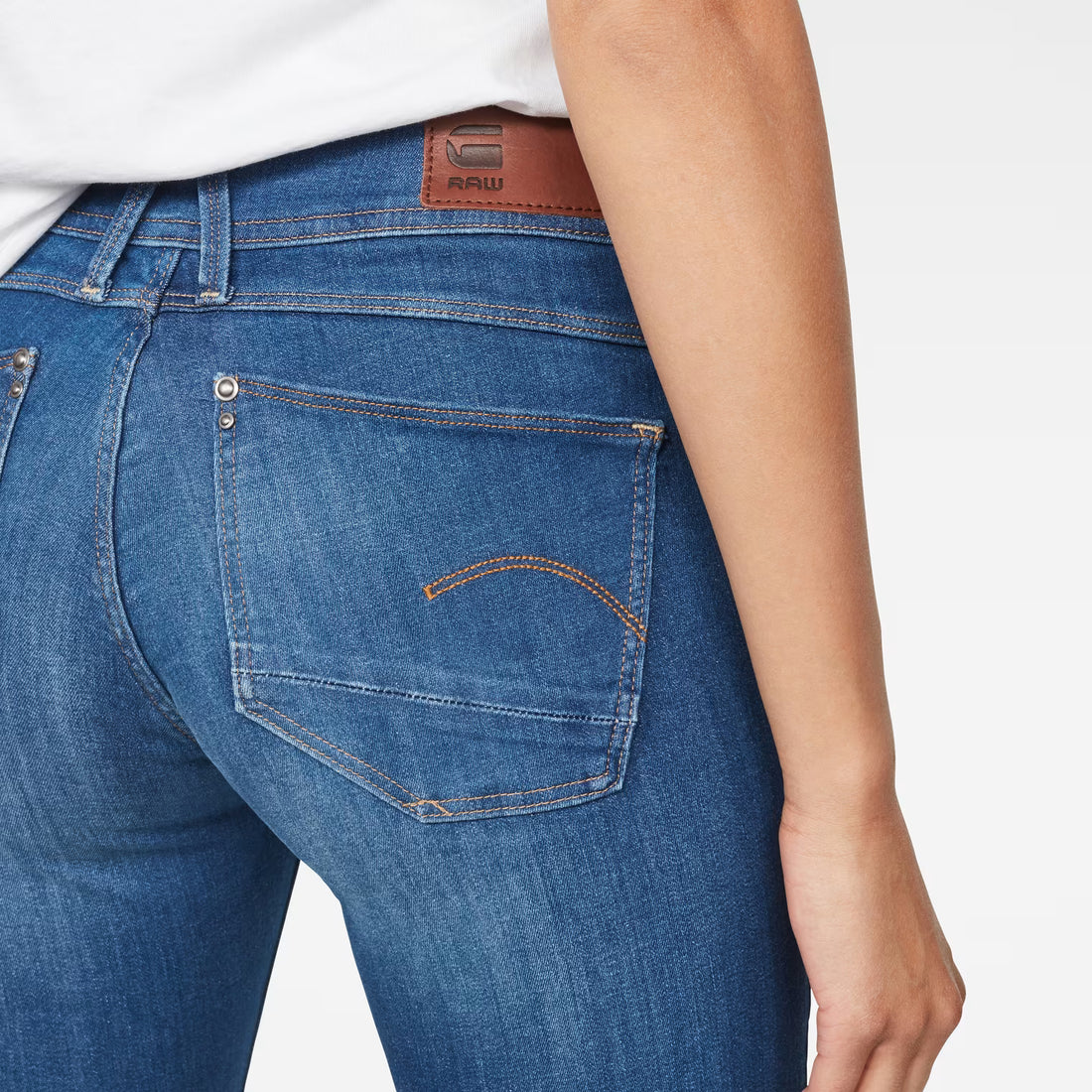 Detail close-up of blue skinny jeans showing back pockets and stitching on a white background